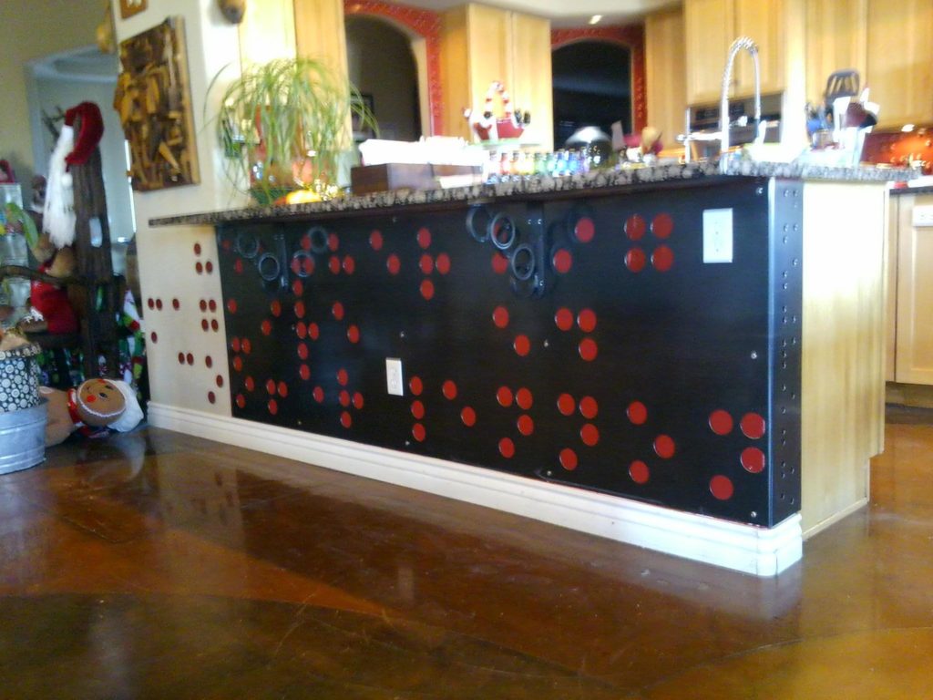 One last installation done before Christmas. This is a piece of hot rolled steel that I machined holes in and faced the pony wall under the granite counter top. The pattern is Braille, and it spells out names. The Braille dots to the left are steel disk that are painted to match the color of the wall behind the steel sheet. Also, on the section that turns the corner there is the Yiddish word for family spelled out in Braille. English Braille though, not Yiddish symbol Braille. The corbel brackets holding up the counter made from circles also have braille on the strip that goes up and down.